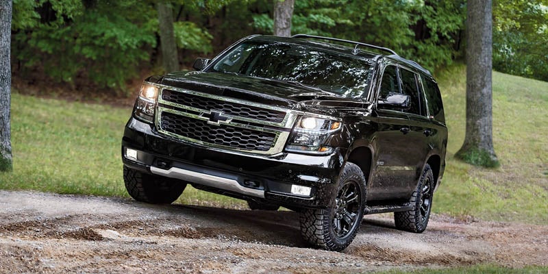 Chevrolet Tahoe running on a paved surface with sand dunes and grass in the background